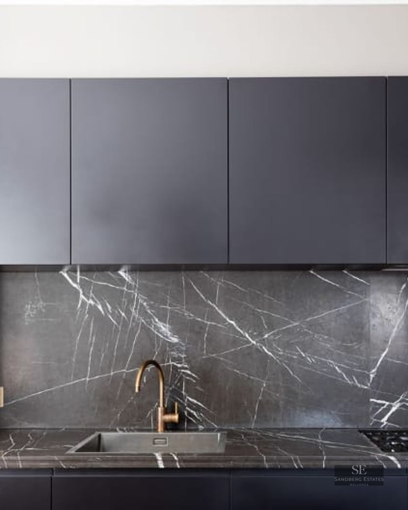 Close-up of a modern kitchen featuring a veined marble backsplash, brass faucet, and black cabinetry.