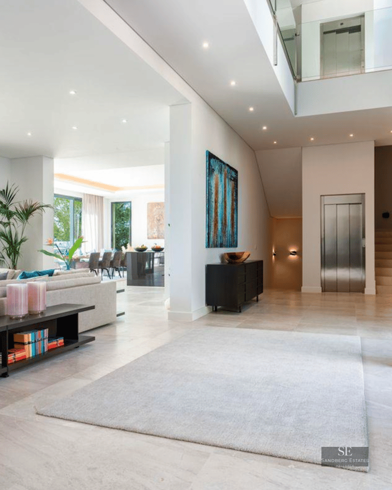 Spacious modern living room with grey sofa, large windows overlooking the sea, and an indoor elevator.