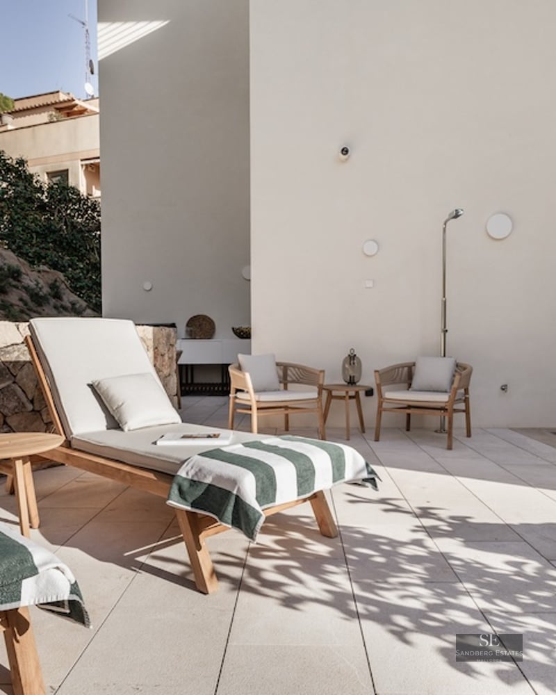 Modern outdoor terrace featuring wooden sunbeds, a small plunge pool, and a natural stone wall in bright sunlight.