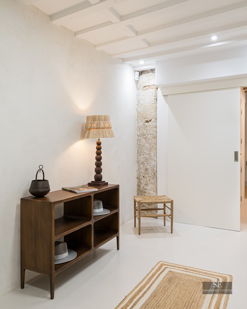 Modern hallway featuring a dark wood console table, exposed stone pillar, abstract art, and a white sliding door.