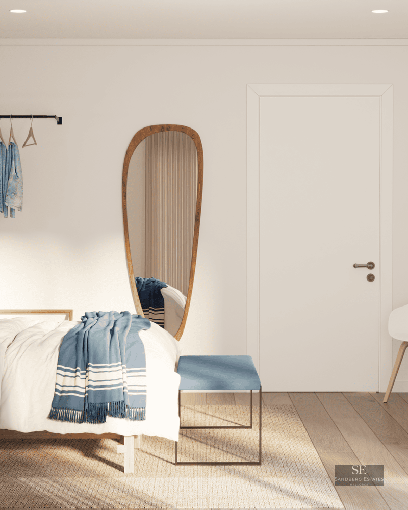 Chambre lumineuse avec lit en bois, literie bleue, miroir de forme organique et meubles en bois clair.