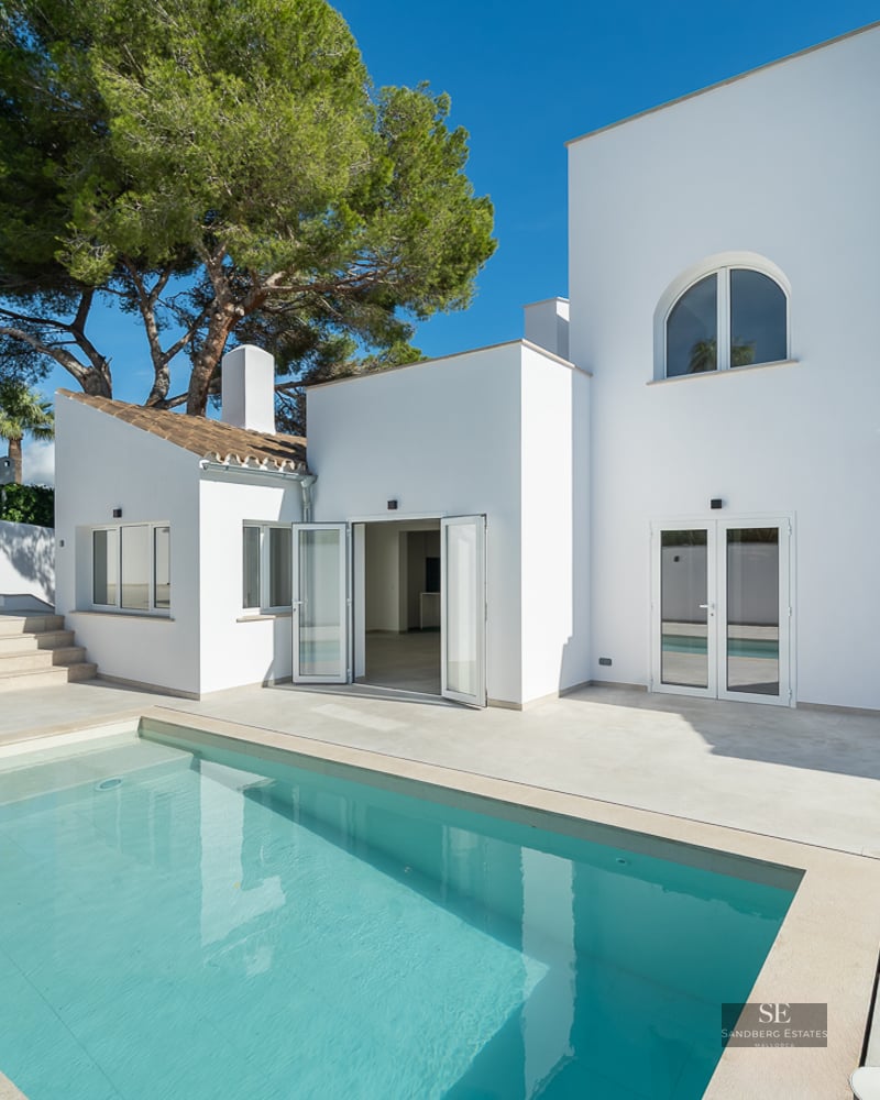 Modern white villa featuring a rectangular swimming pool and sun-drenched terrace under a clear blue sky.