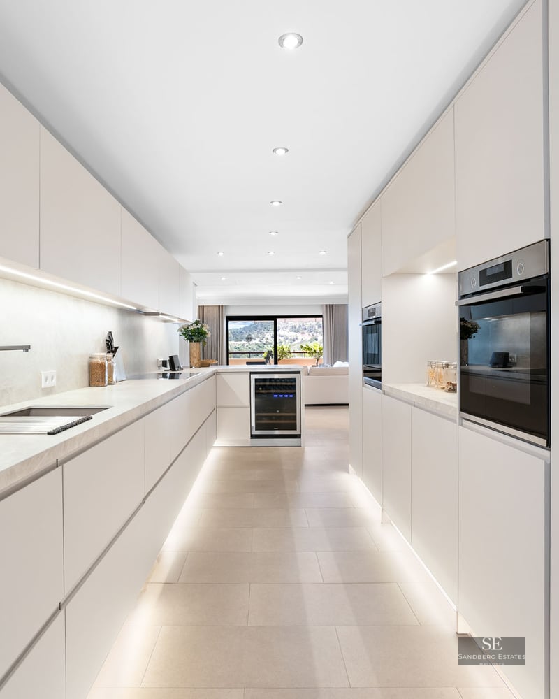 Cuisine moderne avec placards blancs sans poignées, plans de travail en marbre et éclairage LED intégré.