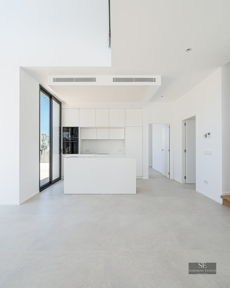 Bright white minimalist kitchen with island, wooden stairs, and large floor-to-ceiling windows.