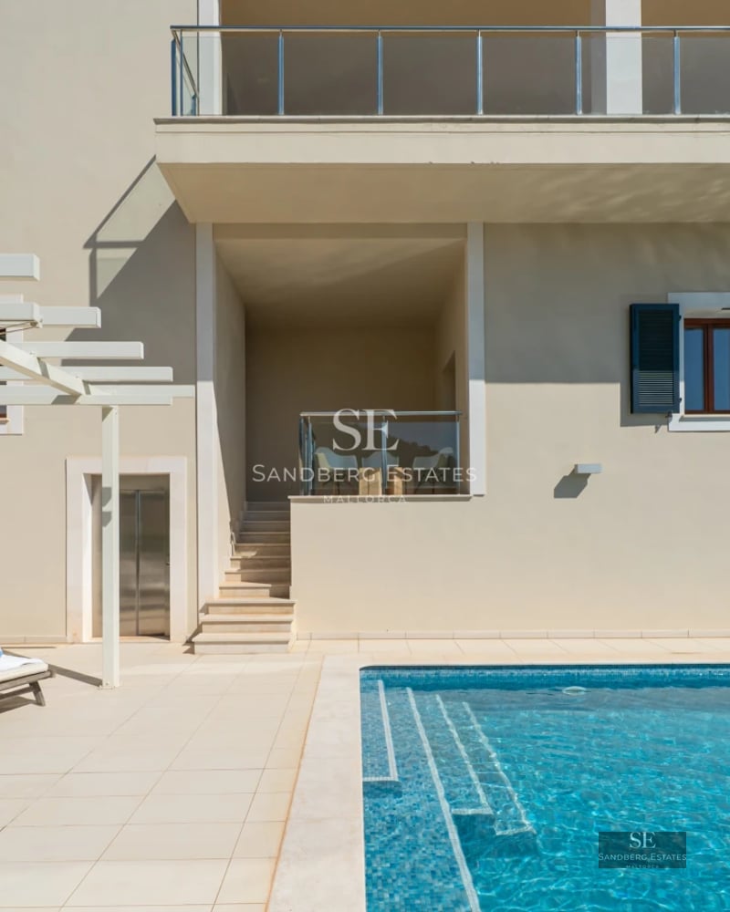 Spacious living room with floor-to-ceiling windows, light wood floors, designer sofas, and direct access to the terrace and pool.