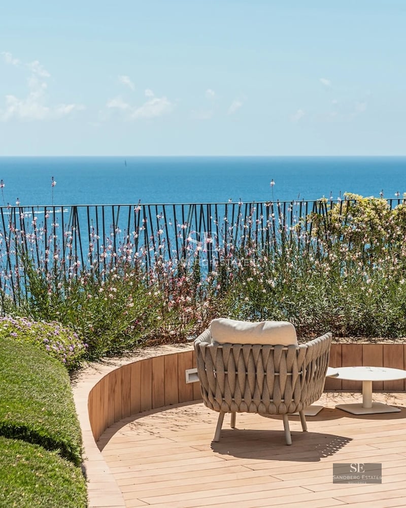 Spacious balcony with panoramic sea views. Modern design, glass railing, and tiled floor. Soft lighting and stylish furniture.