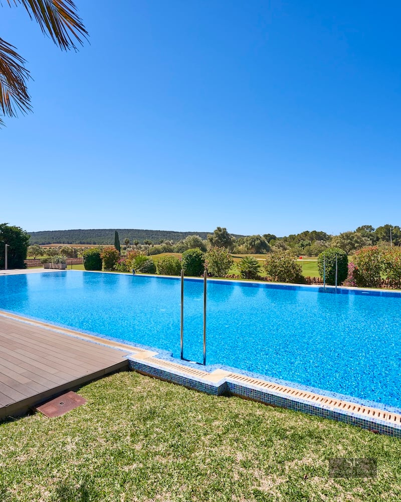 Blue rectangular pool with a wooden deck, green lawn, and landscape views under a clear blue sky.