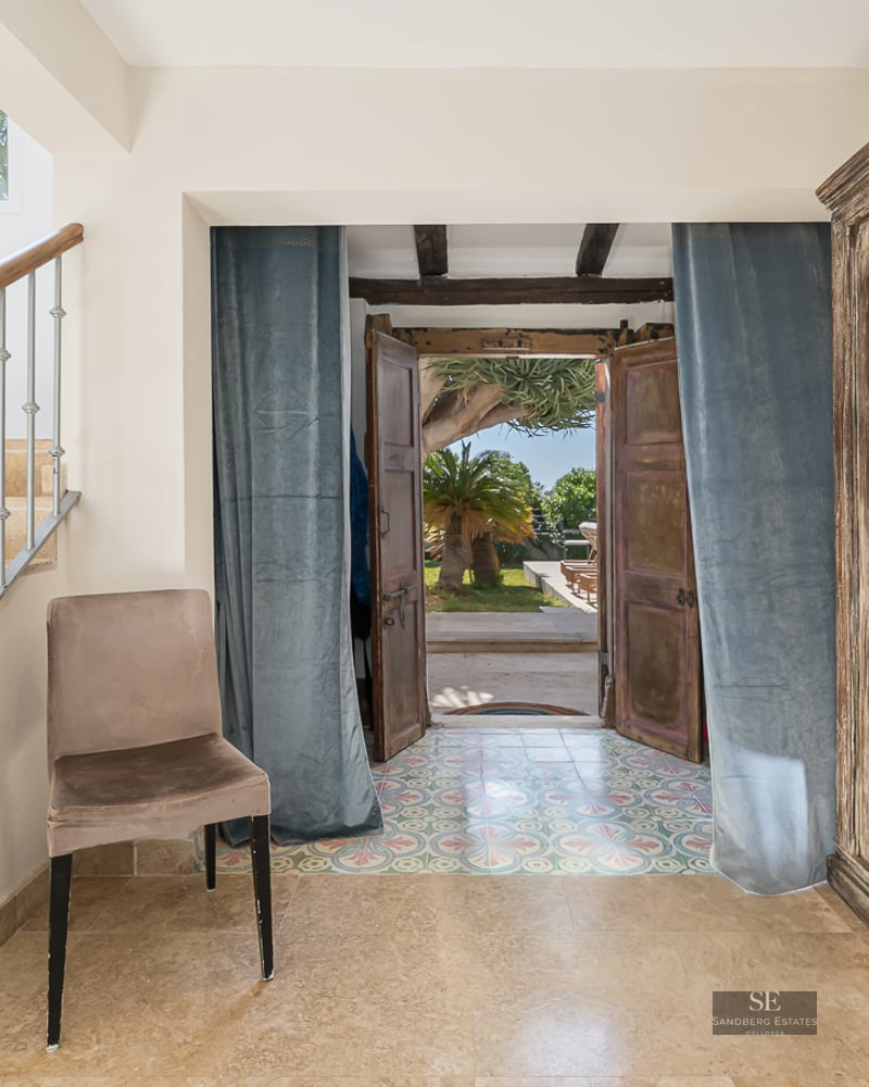 Entrance hall featuring a stone staircase, large antique wooden cabinet, and open doors leading to a sunny garden.