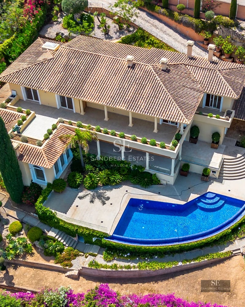 Exterior view of a modern villa featuring an infinity pool, large windows, and minimalist architecture. Lush garden and clear skies.