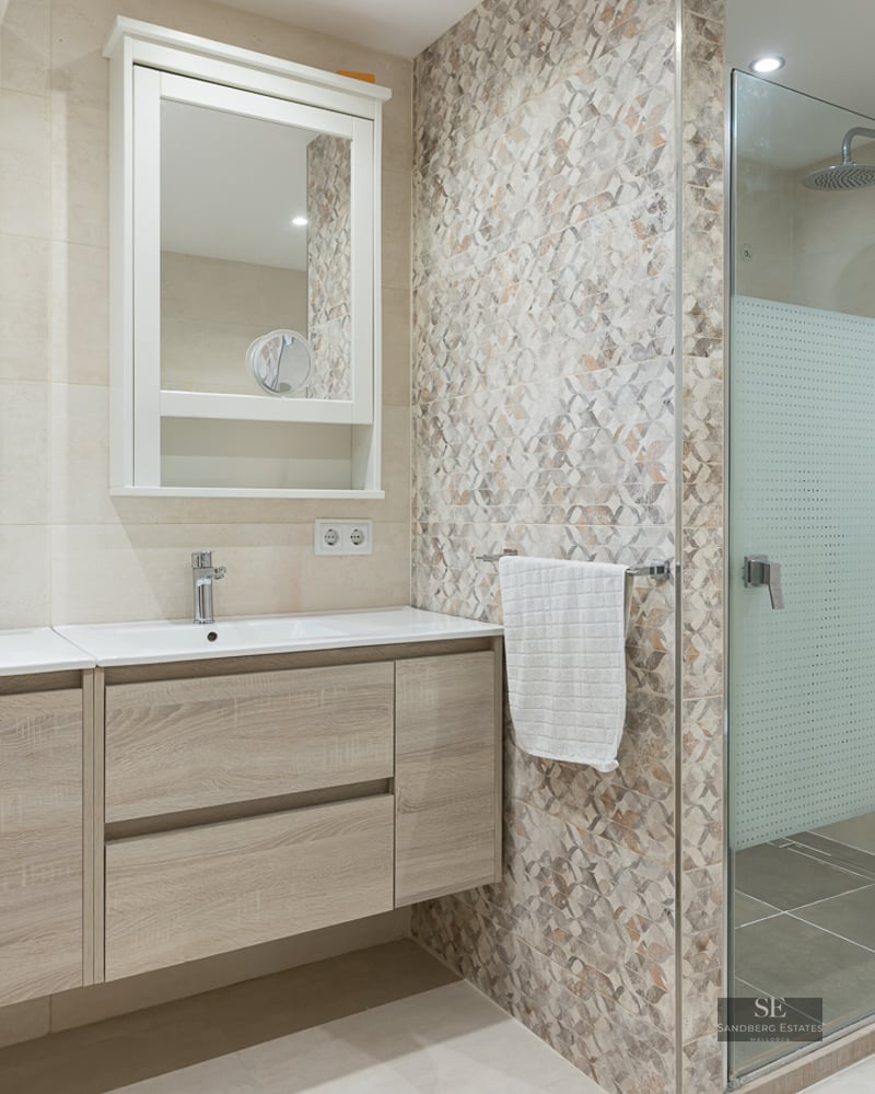 Bright master bathroom featuring a light wood double vanity, two mirrors, and a glass-enclosed walk-in shower.
