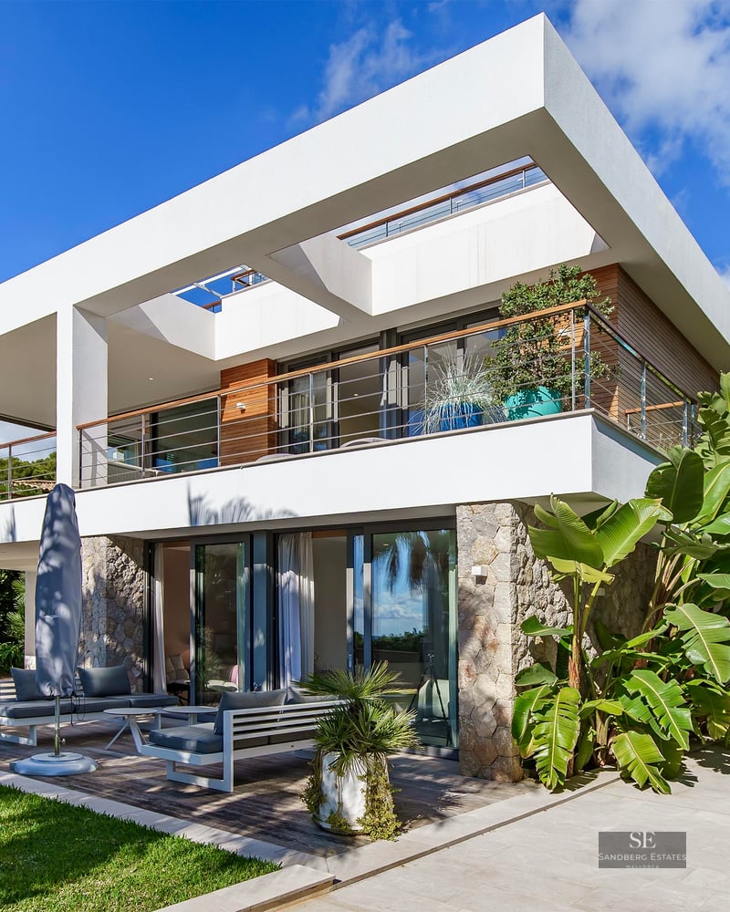 Villa moderne blanche sur deux niveaux avec pierre naturelle et jardin tropical sous un ciel bleu.