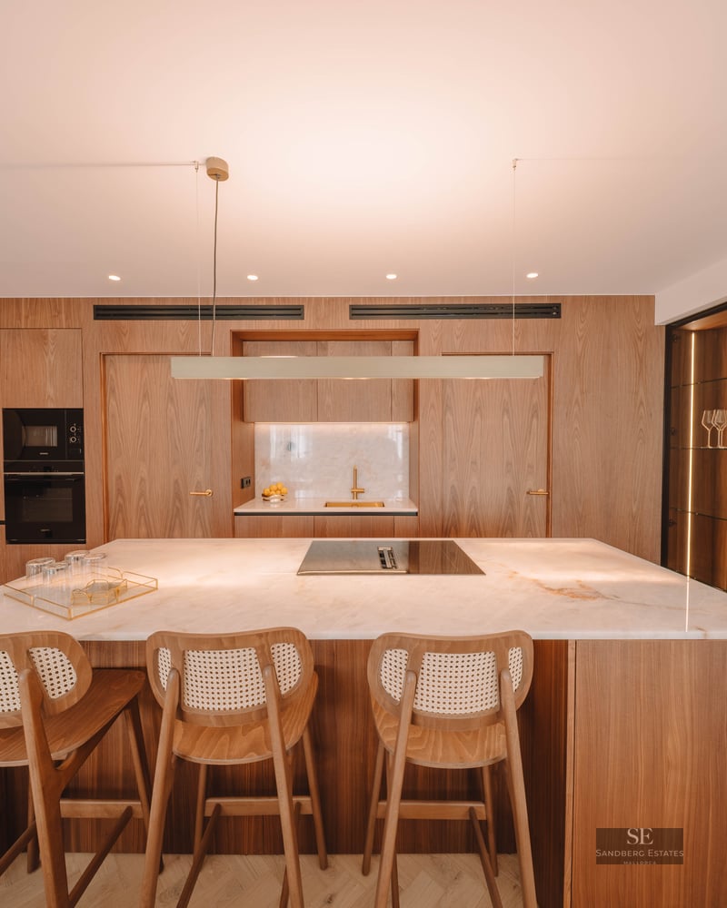 Modern kitchen featuring a white marble island, wood bar stools, and floor-to-ceiling warm wood cabinetry.