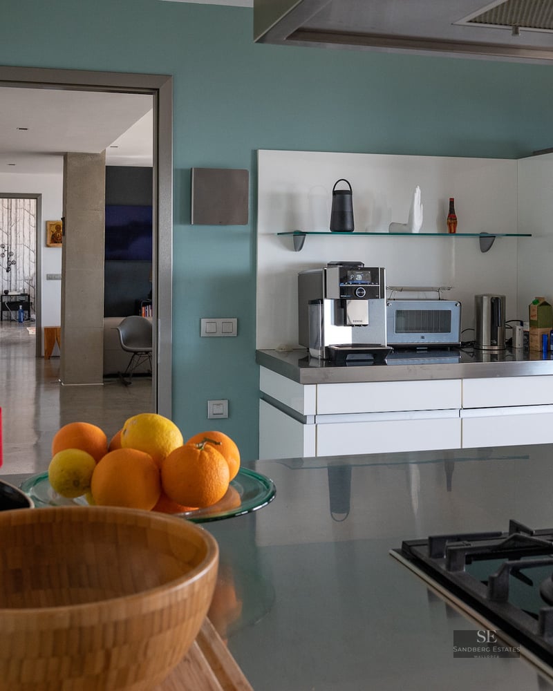 Modern kitchen featuring stainless steel countertops, a professional espresso machine, gas stovetop, and fresh citrus fruit.