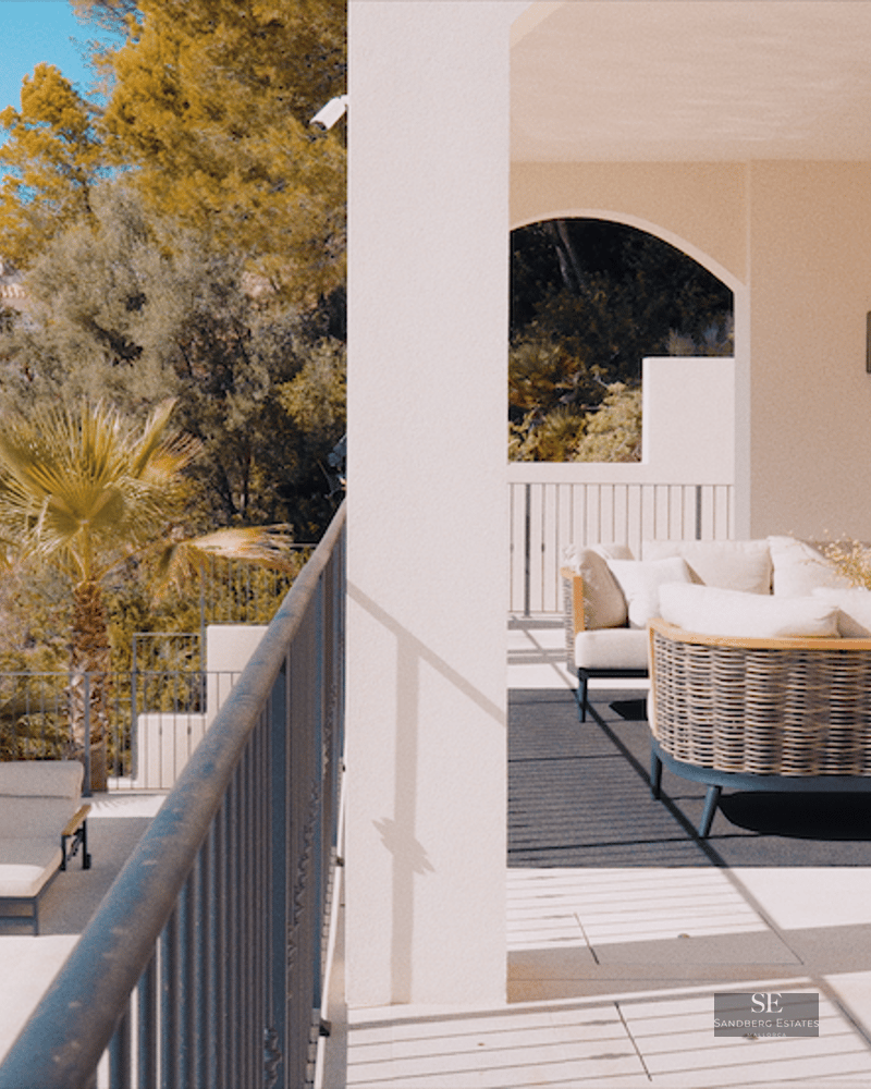 Sun loungers and a white umbrella on a stone terrace overlooking a Mediterranean hillside town.