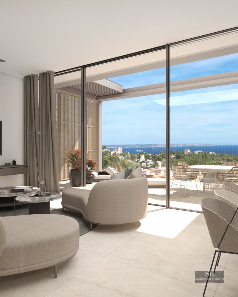 Bright modern living room with curved beige sofas and floor-to-ceiling glass doors opening to a terrace with sea views.