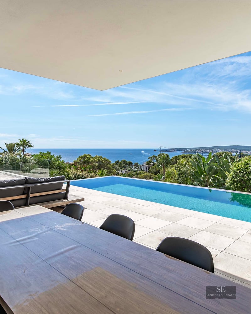 A modern luxury terrace featuring an infinity pool overlooking the ocean, with outdoor dining and lounge seating.