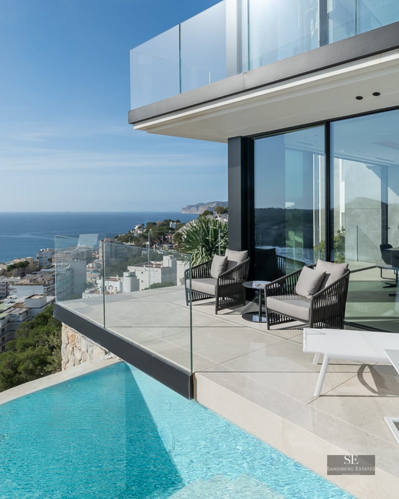 Modern terrace featuring a turquoise infinity pool, white sun lounger, and glass railings overlooking the Mediterranean sea.