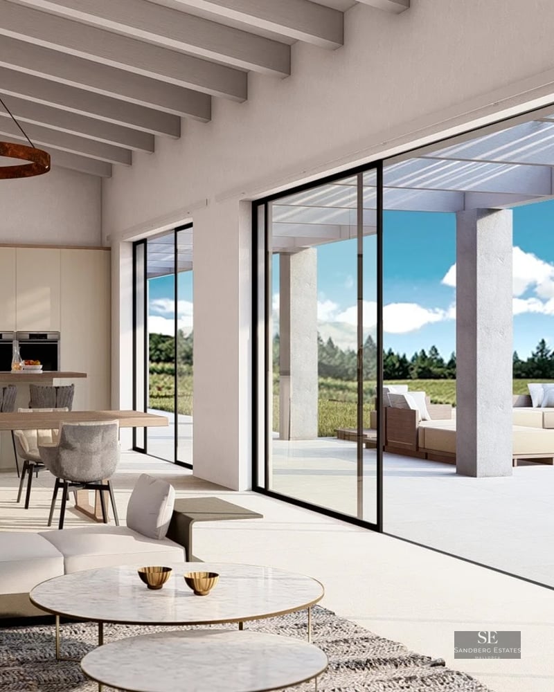 Bright living room with wooden beams, modern sofas, and large glass sliding doors opening to a sunny terrace.