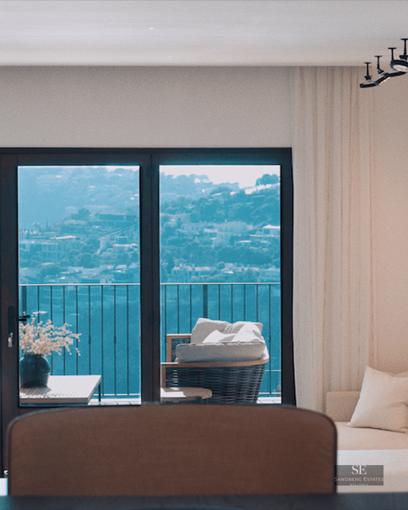 Bright living room with white sofa and large windows overlooking a scenic hillside and balcony furniture.