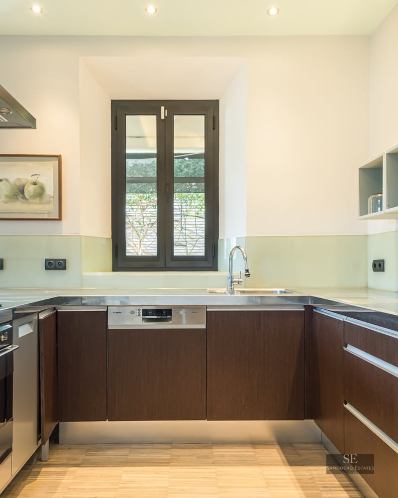 Modern kitchen with dark wood cabinets, stainless steel countertops, and a glass backsplash under bright lighting.