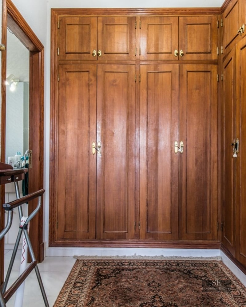 Walk-in closet with floor-to-ceiling wooden built-in wardrobes, Persian rug, and a valet stand.