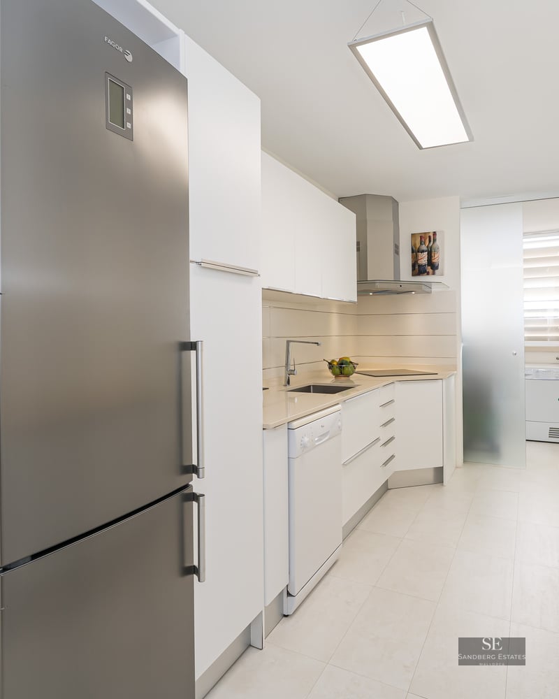 A modern galley-style kitchen with white cabinetry and stainless steel appliances.