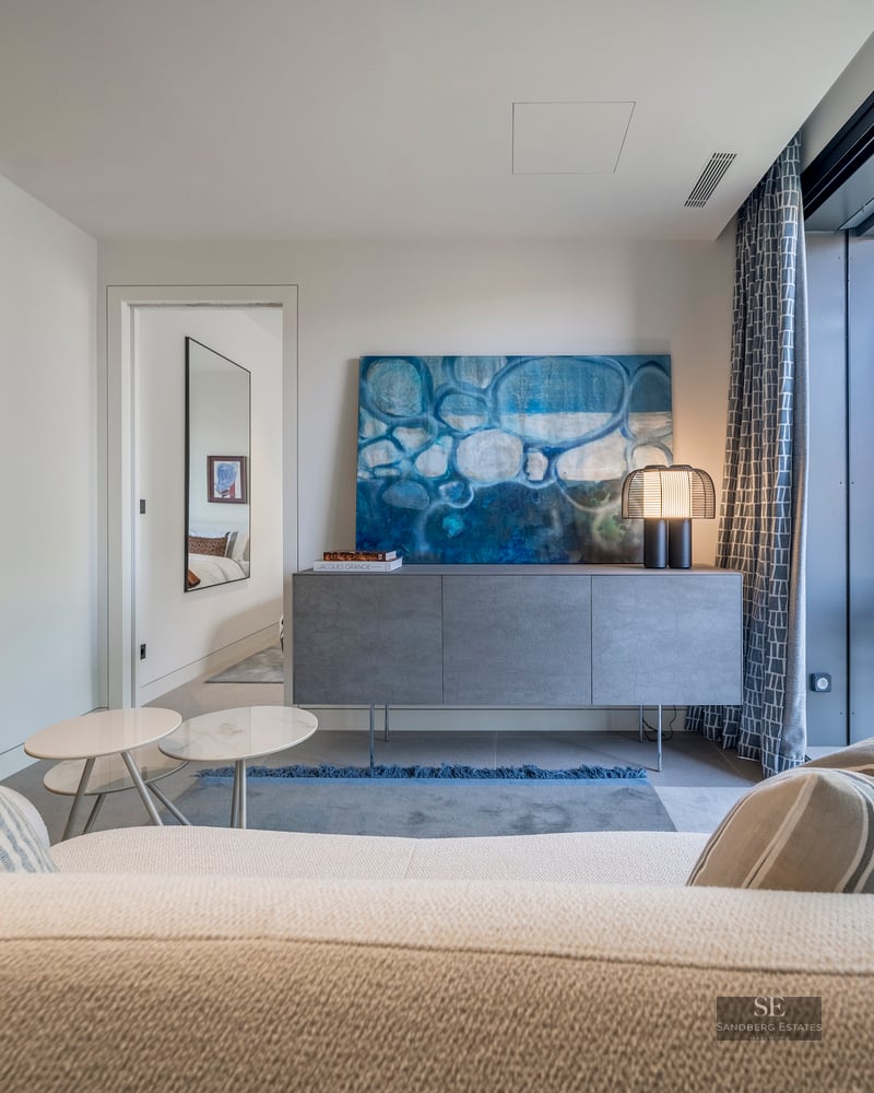 Modern living room featuring a white bouclé sofa, blue abstract art, and large glass doors to a terrace.