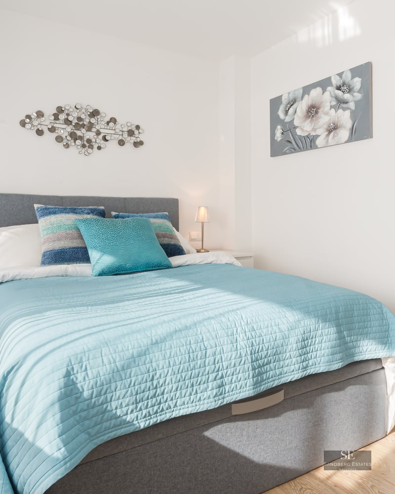 Chambre lumineuse avec lit turquoise, tête de lit grise et salle de bain privative visible en arrière-plan.