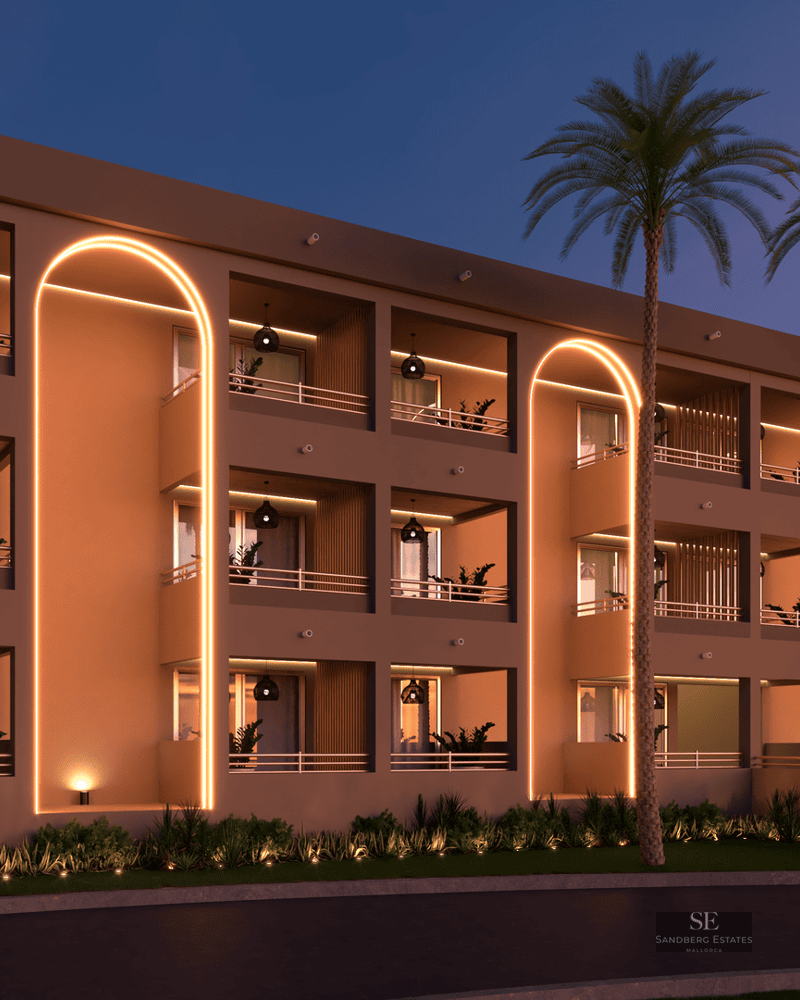 Bâtiment moderne avec arches dorées illuminées, balcons privés et palmiers sous un ciel de crépuscule.