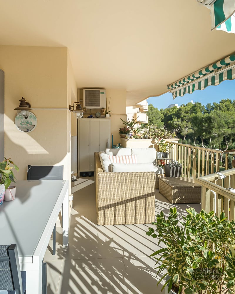 Grand balcon carrelé avec table à manger extérieure, canapé en osier et store à rayures vertes et blanches.