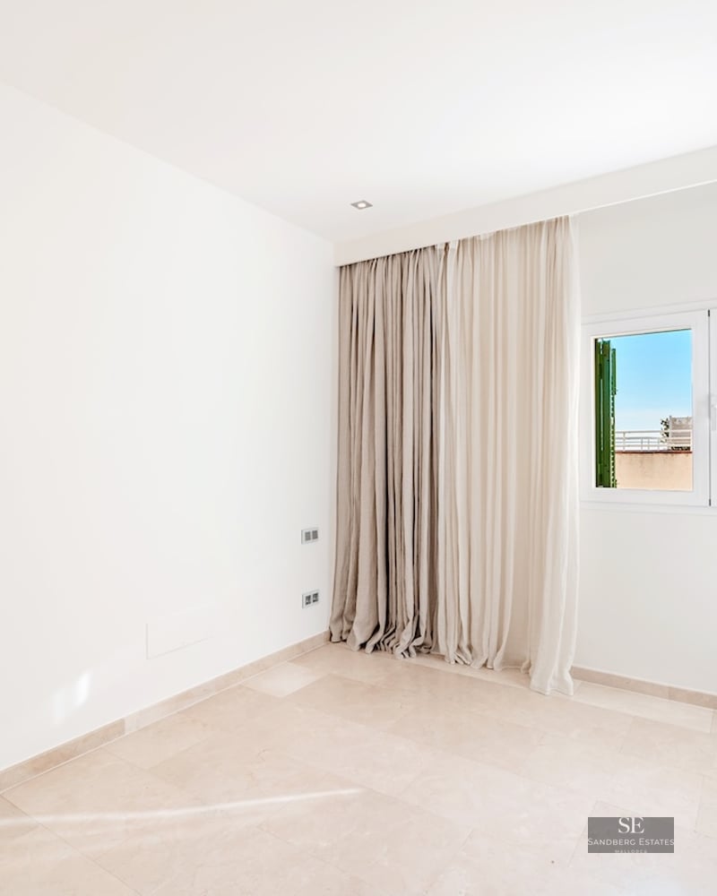 Empty bright room with white walls, polished beige stone floors, a large window with floor-to-ceiling curtains.