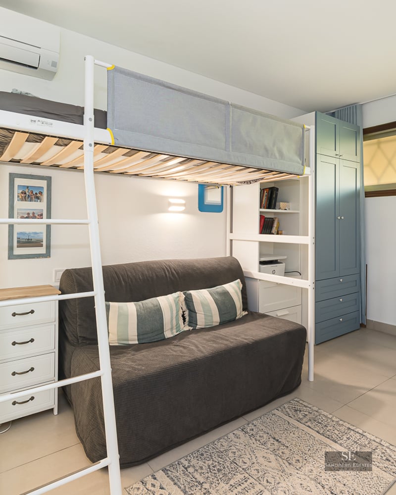 Lit mezzanine en métal blanc au-dessus d'un canapé gris, à côté d'un bureau et d'une armoire bleue.