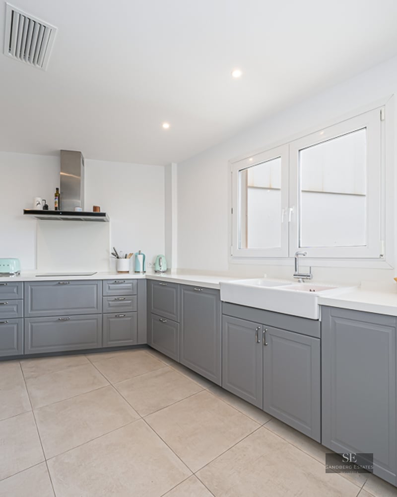 Cuisine lumineuse avec placards gris style shaker, plans de travail blancs et grand évier timbre d'office.