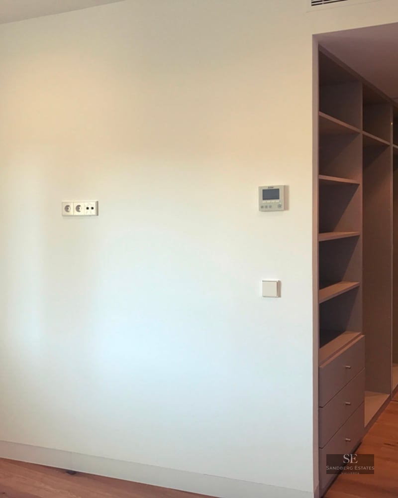 White room with light wood floors and a grey built-in shelving and drawer unit leading into a hallway.