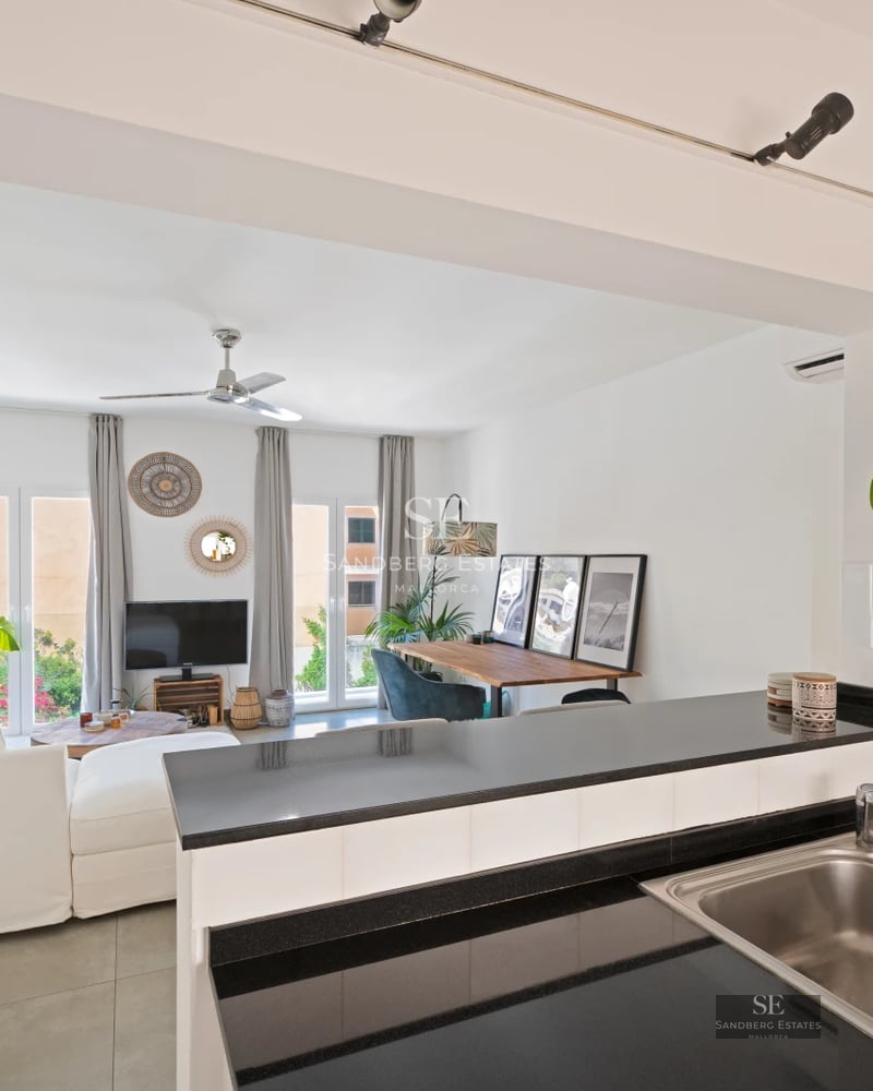 Spacious balcony overlooking the sea. Wooden floors, glass railing, modern outdoor furniture. Clear blue sky.