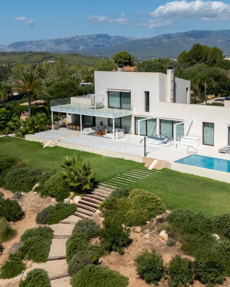 Exterior view of a modern villa featuring an infinity pool, large windows, and lush gardens. Minimalist architecture.