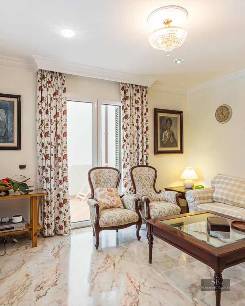 Living room featuring a plaid sofa, floral armchairs, wooden coffee table, and polished marble flooring.