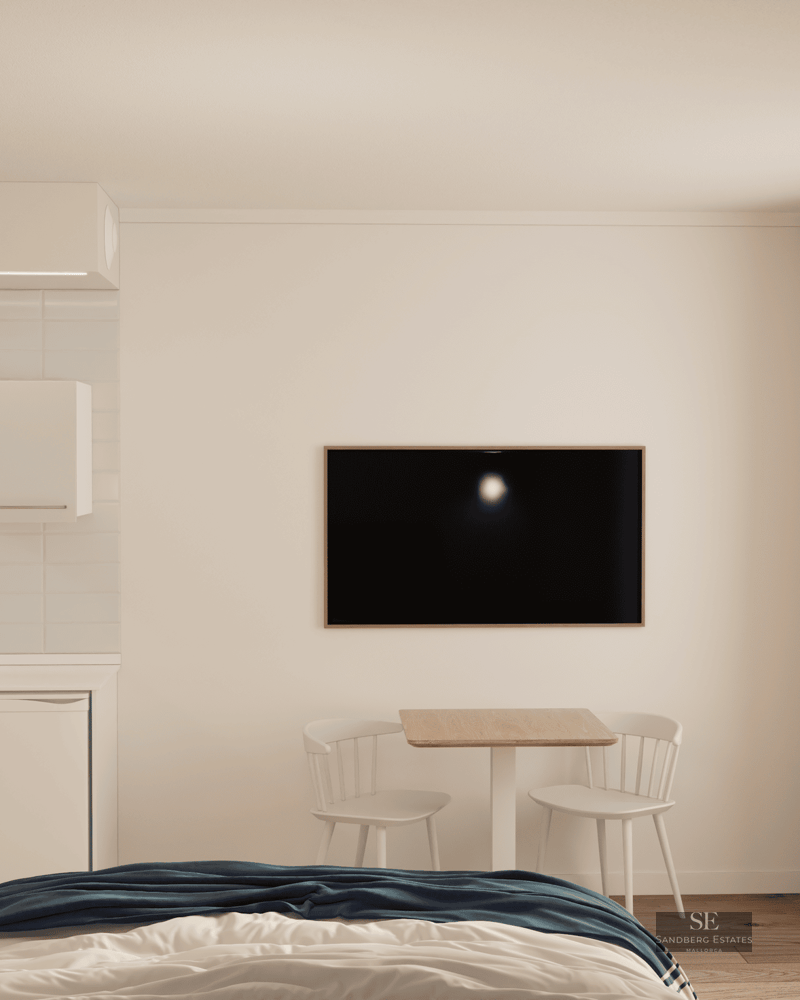 Modern studio featuring a bed, dining area, small kitchen, and balcony access under soft natural light.