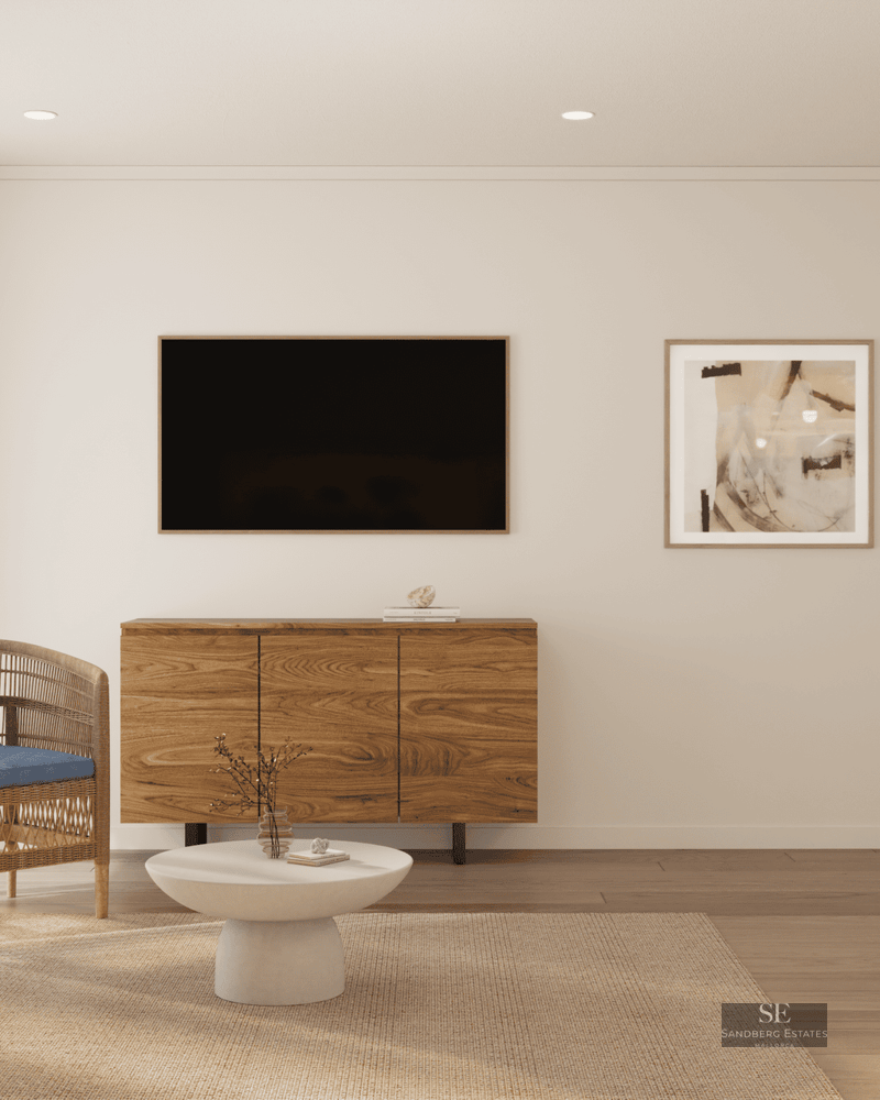 Bright living room featuring a wooden sideboard, wall-mounted TV, wicker chair, and white coffee table on a rug.