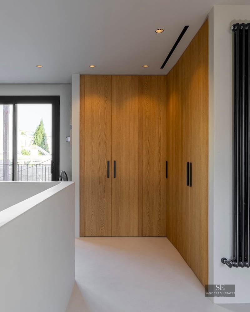 Couloir avec armoires en bois du sol au plafond, radiateur noir vertical et porte vitrée menant au balcon.