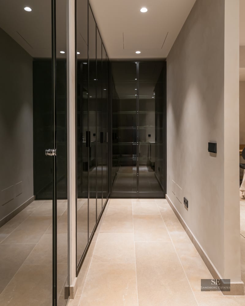 Minimalist master bedroom featuring sleek dark glass wardrobes, stone tile flooring, and warm recessed lighting.