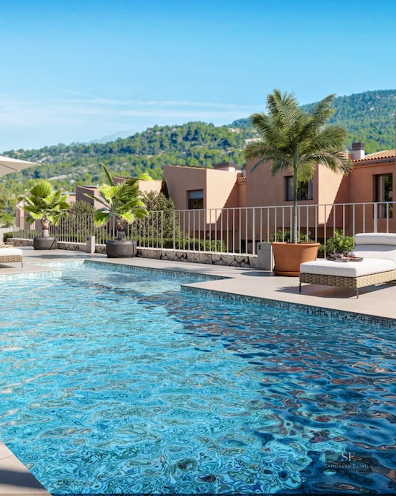 Turquoise swimming pool with sun loungers and palm trees overlooking lush green mountains under a blue sky.