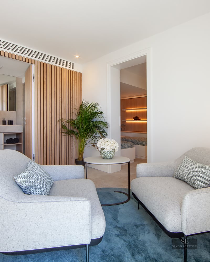 Master bedroom suite featuring two grey armchairs, blue rug, wooden slat wall, and view of the bedroom area.