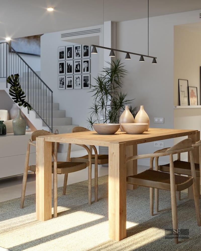 Contemporary dining area with a light wood table, four woven chairs on a grey rug, and a modern staircase in the background.