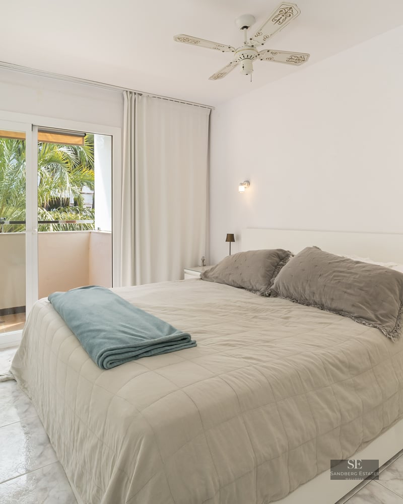 Bright bedroom with double bed, marble floors, and balcony doors showing palm trees.