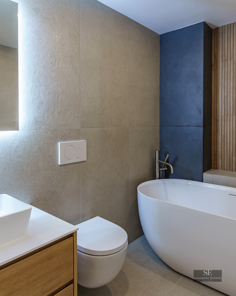 Salle de bain moderne avec baignoire îlot, vasque sur meuble en bois et miroir rétroéclairé.