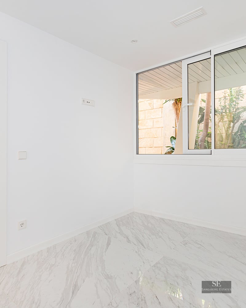 Empty room with white walls, polished marble floor, and a large sliding window overlooking outdoor greenery.