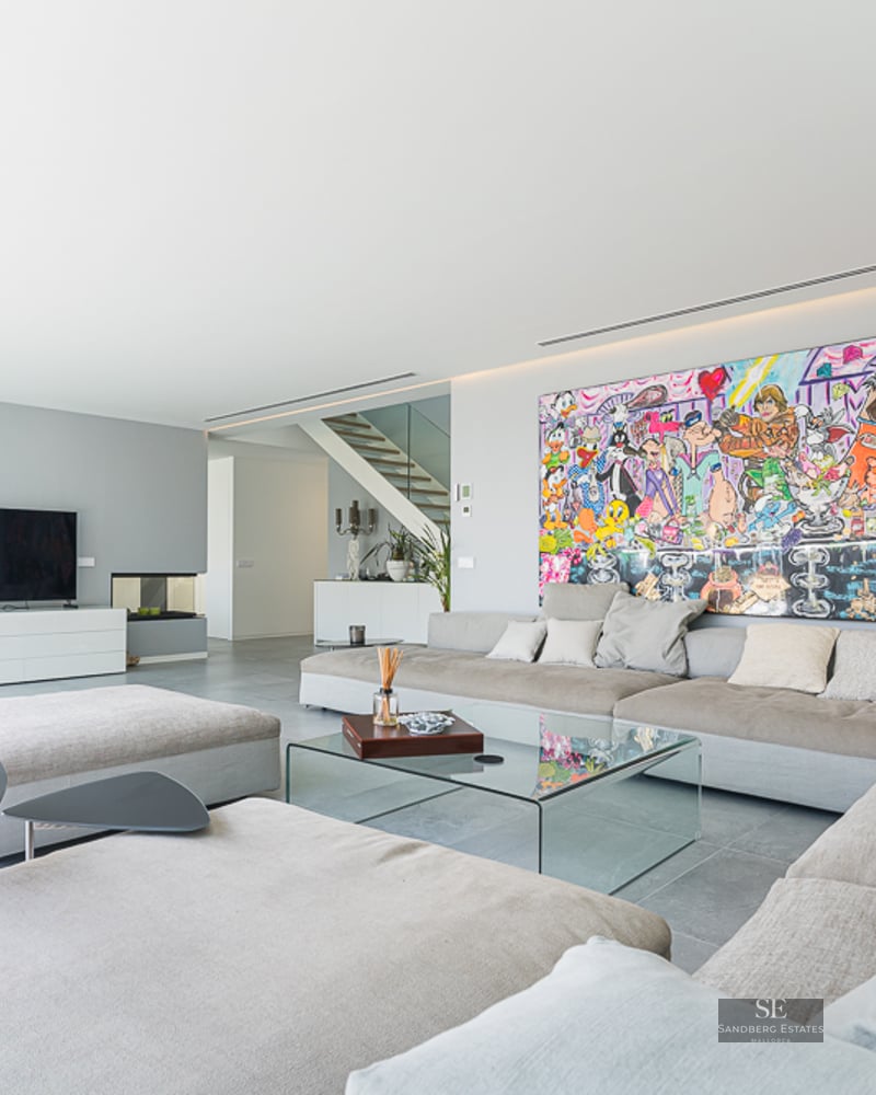 Modern living room with large beige sofa, glass table, and a massive colorful cartoon painting on a white wall.
