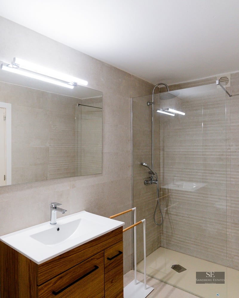Contemporary bathroom featuring a walk-in glass shower, stone tiles, and a wooden vanity with a large mirror.