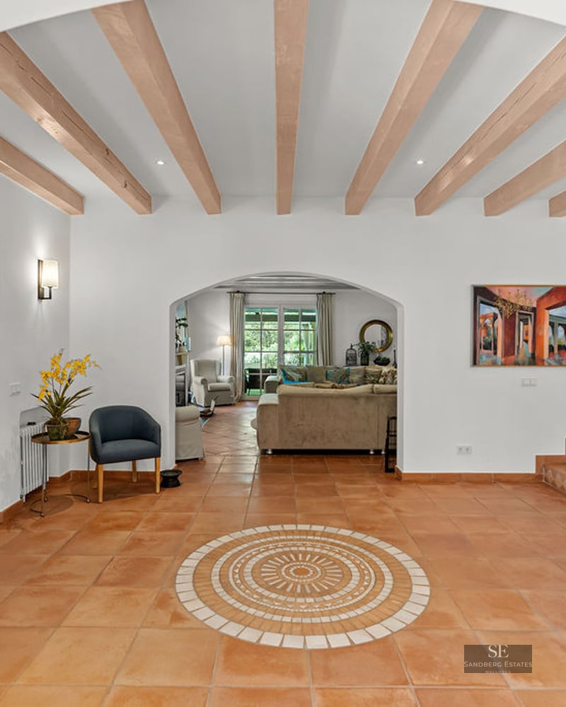 Entryway with wooden ceiling beams, terracotta floors, an arched doorway to the living room, and a tiled staircase.